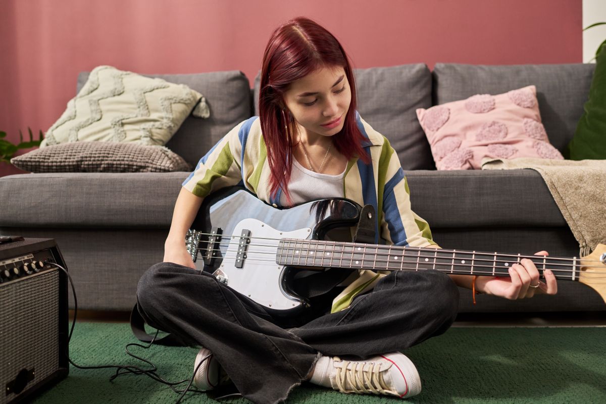 A female teen playing Bass Guitar with headphones plugged into her laptop